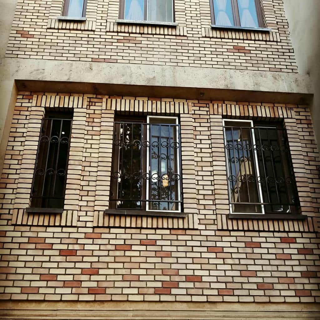 نرده پنجره مشکی کنار نمای آجری باران خورده